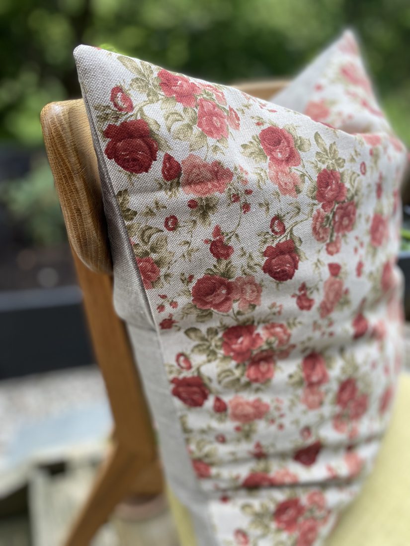 Blommig kudde i rosmönstrat tyg draperad över en trästol utomhus
